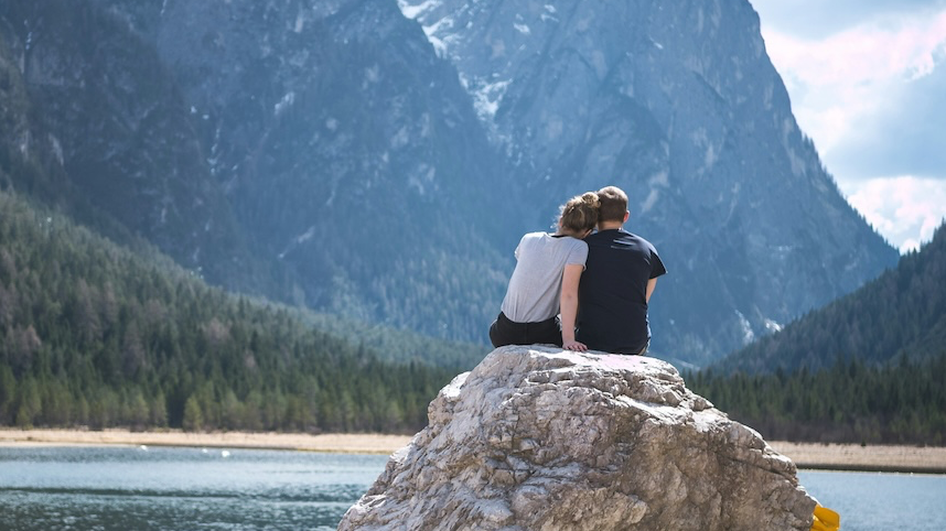 Couple sitting together on rock in front of lake and mountains