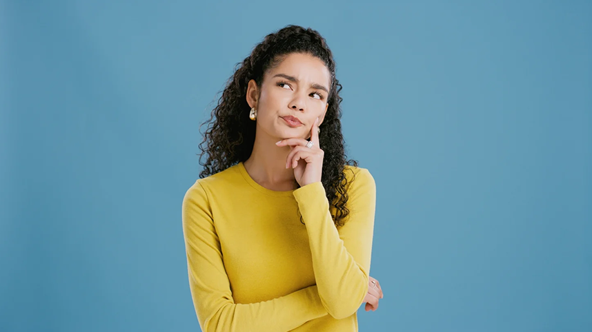 Person in yellow sweater with hand on chin looking up and thinking