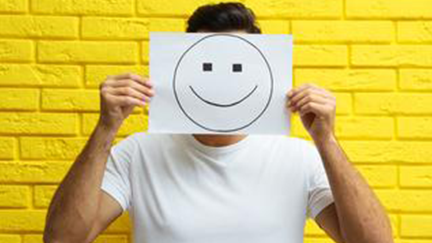Person holding up drawing of a smiley face over their own face