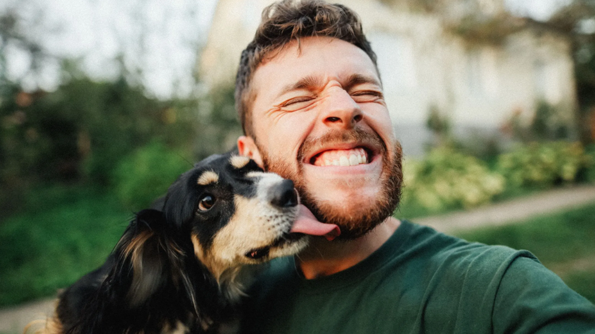 Man smiling as his dog licks face