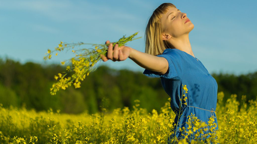 Person in field of yellow flowers, eyes closed, arms outstretched